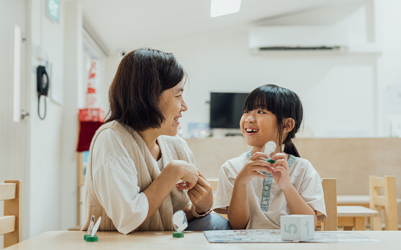 A supportive teacher at Little Seeds Preschool smiling and engaging with a young student