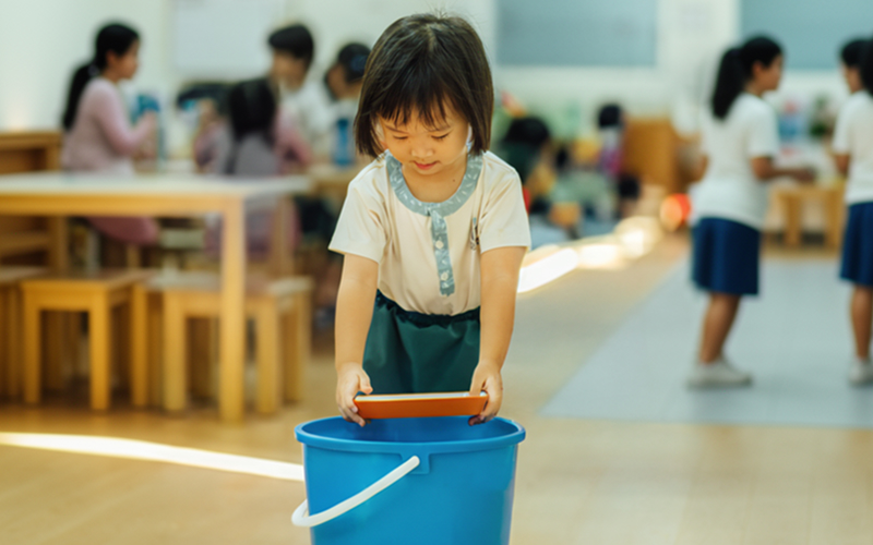 Young girl focused on placing a thing into a blue bucket.