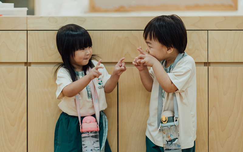Two young children interacting and gesturing playfully at each other.