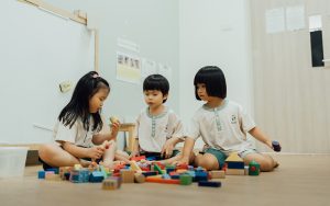 Three preschool children sitting together and playing with wooden blocks.