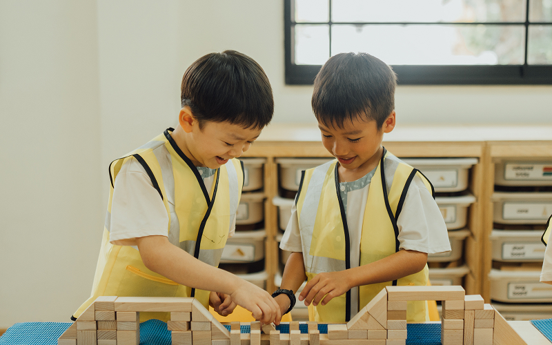 Two young boys in safety vests playing with wooden blocks.