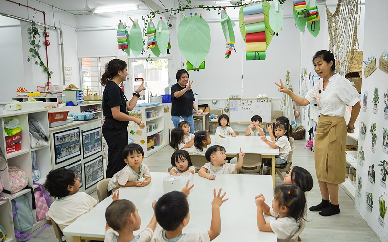 Teachers and students interacting at tables in a decorated classroom.