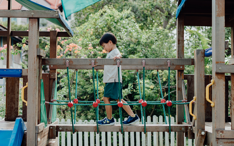Young boy building confidence on a playground bridge.