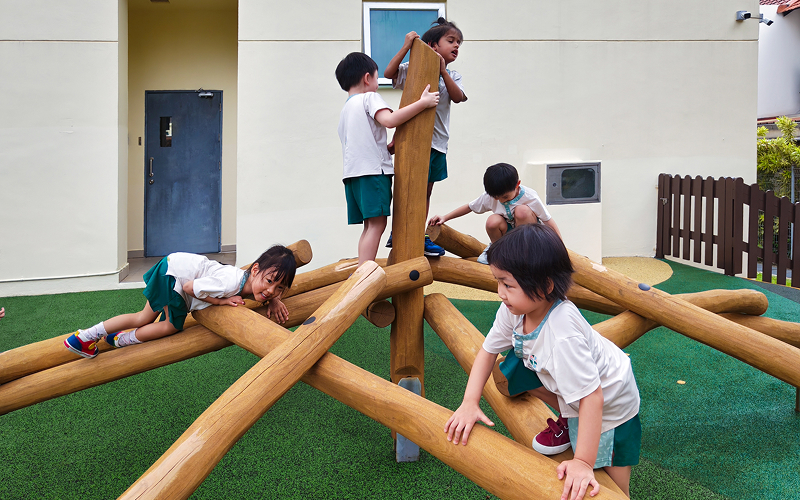 Young children playing on outdoor wooden climbing structure at preschool.