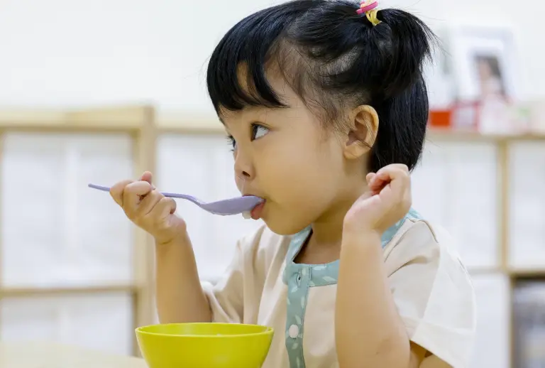 Toddler eating with a spoon at Little Seeds Preschool